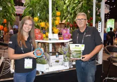 Kara Badder and Ray Wowryk with NatureFresh Farms stand in front of the greenhouse. Kara shows TomZ tomatoes while Ray shows mini cucumbers in a pouch bag.